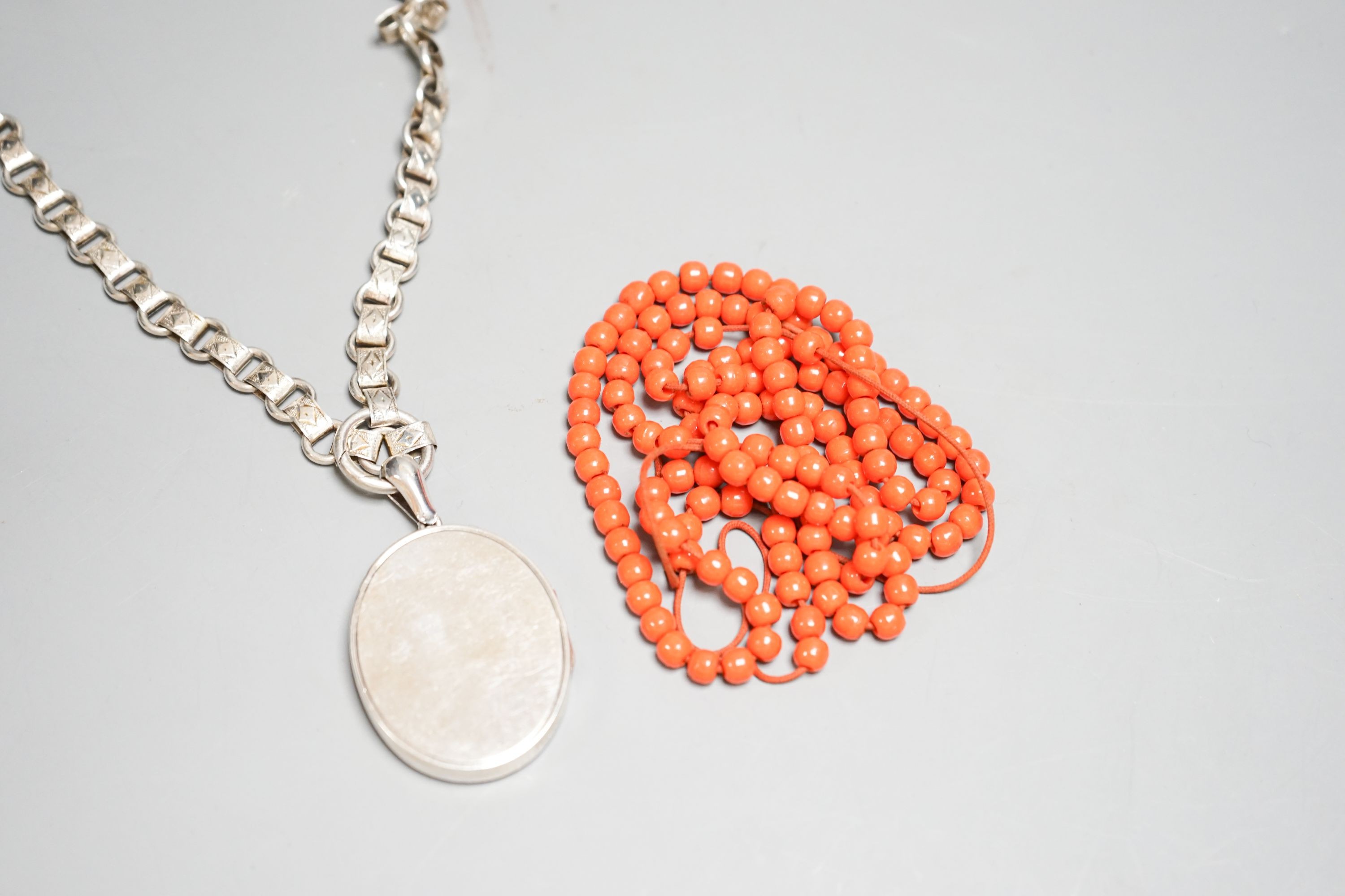 A white metal oval locket with monogram, 43mm, on a fancy white metal chain and a string of coral coloured glass beads.